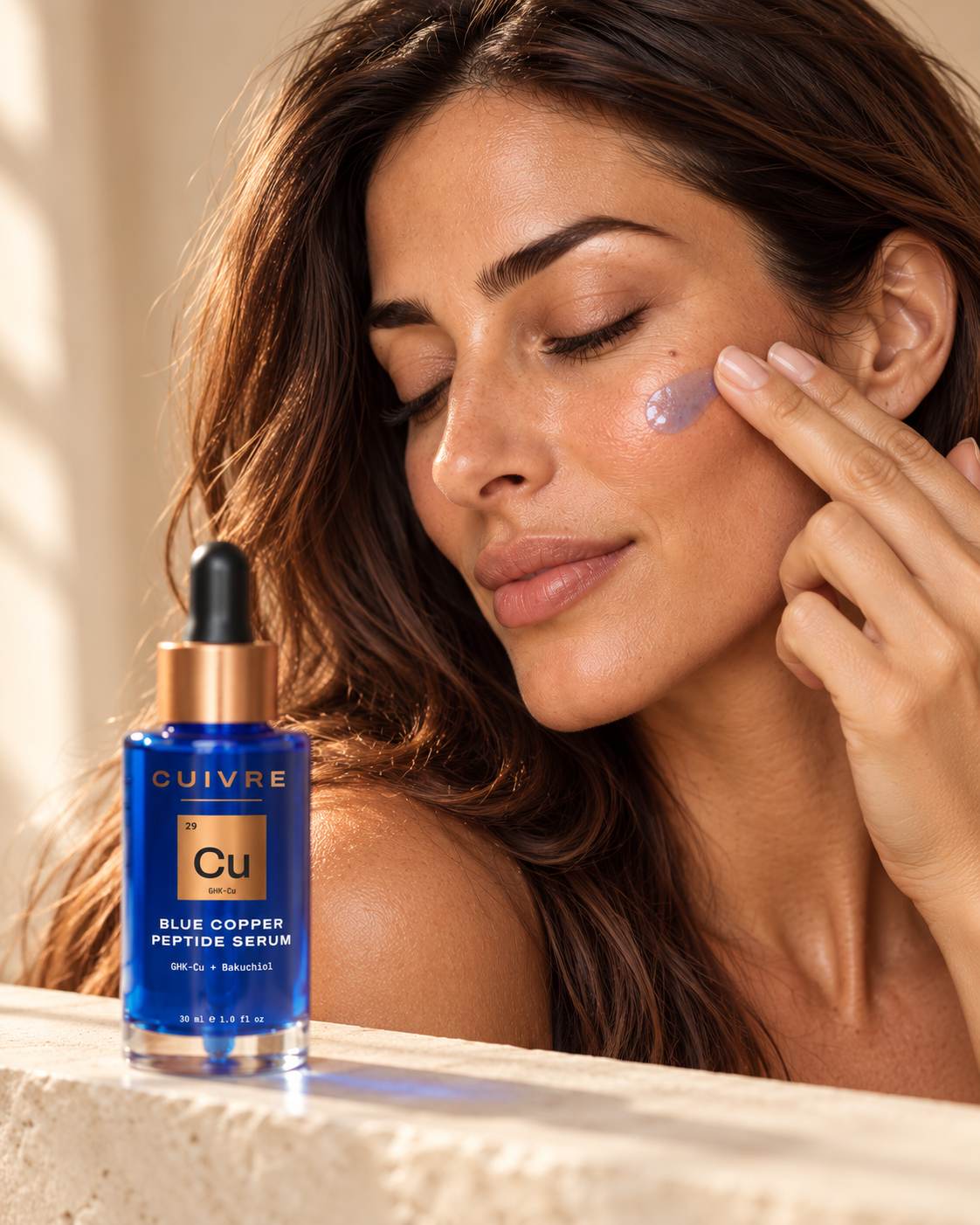 Woman with eyes closed pressing blue copper serum onto her cheekbone, the CUIVRE bottle on a stone ledge in front of her