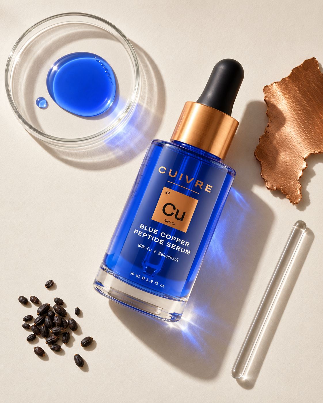 Flat-lay of the CUIVRE serum bottle with a dish of blue copper serum, a swatch of copper, babchi seeds and a glass pipette